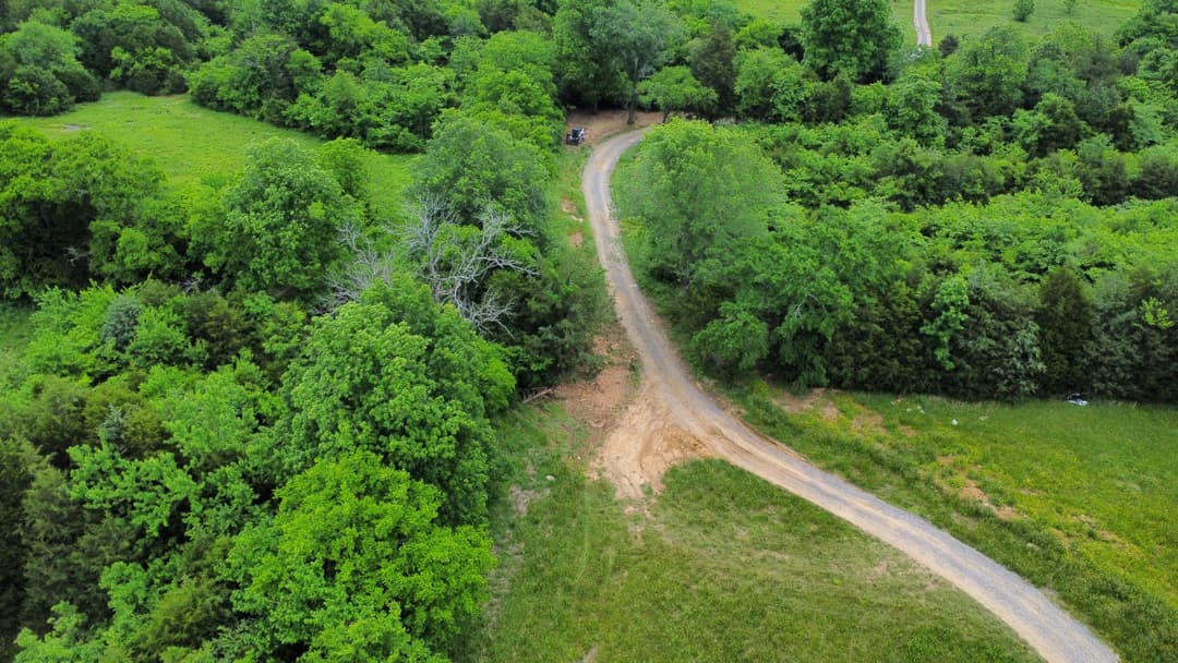 Aerial view of a winding dirt road surrounded by lush green trees and fields.